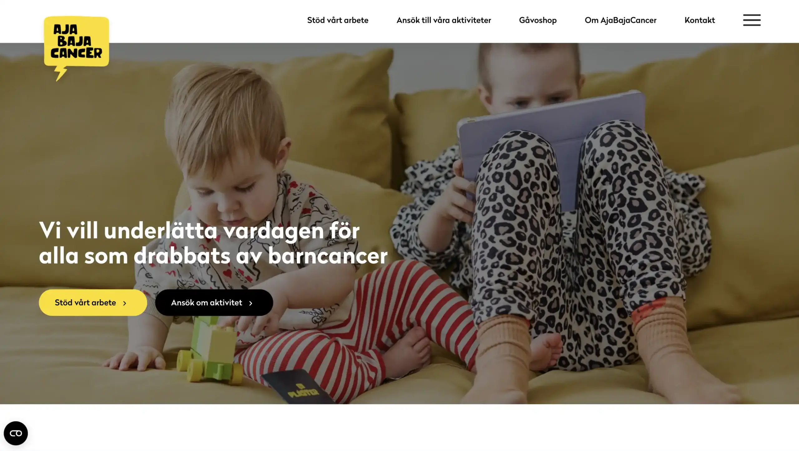 Skärmbild över startsidan på AjabajaCancer. En bakgrundsbild på barn som tittar på en surfplatta och leker. Mörkare overlay med text på bilden och knappar för ingångar. Tonerna går i gult, svart och vitt.