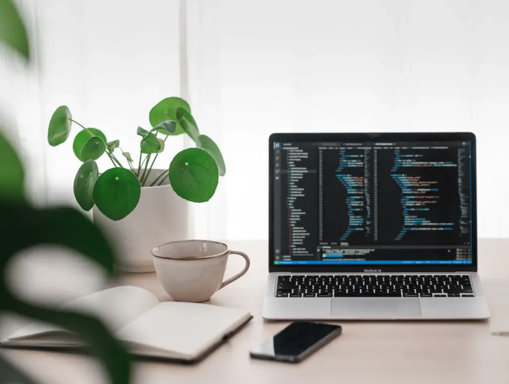 Dator med kod på skärmen, anteckningsblock och kaffekopp - arbetsmiljö för webbutveckling och CRO.