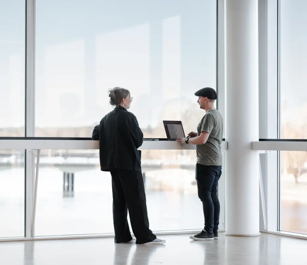 Johan Lindén och Cecilia Ljungquist på webbyrån Decision By Heart står vid en dator med utsikt över Klarälven - i samtal om vidareutveckling av webbprojekt.