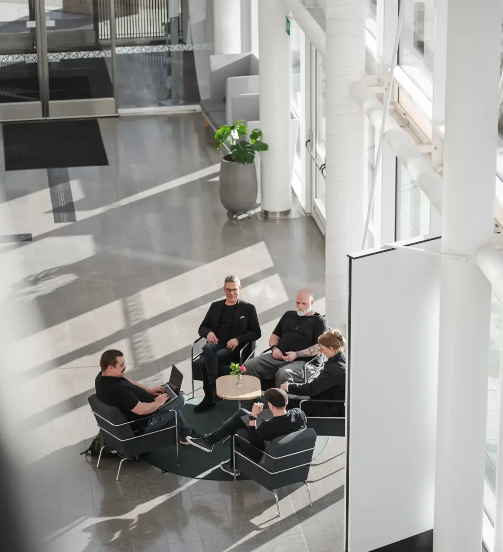 Medarbetare ur teamet sitter i soffor vid ett litet bord i ett möte om web cycle management. 